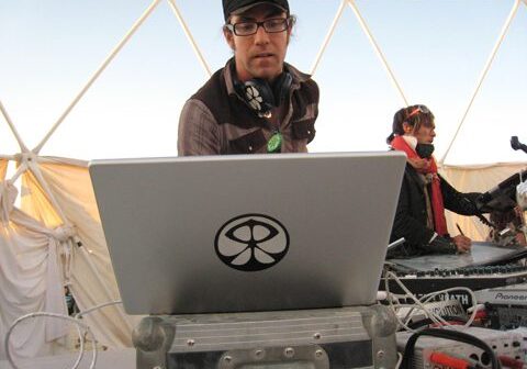DJ performing with laptop and headphones outdoors.