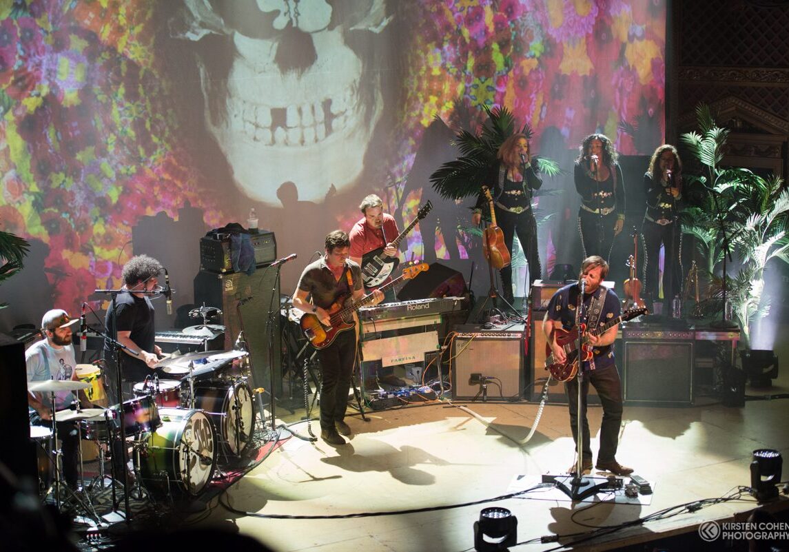 Band performing live with colorful stage backdrop.