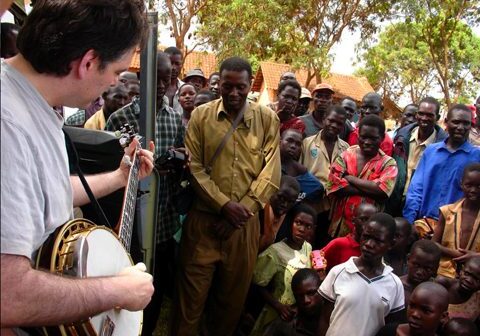 Musician playing banjo for gathered crowd outdoors.