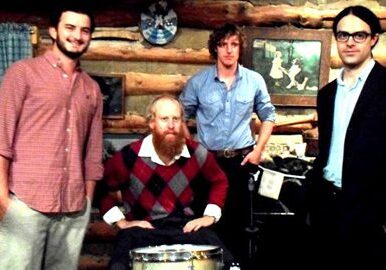 Four men posing in a rustic room.
