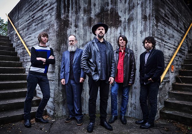 Five men standing against concrete wall.