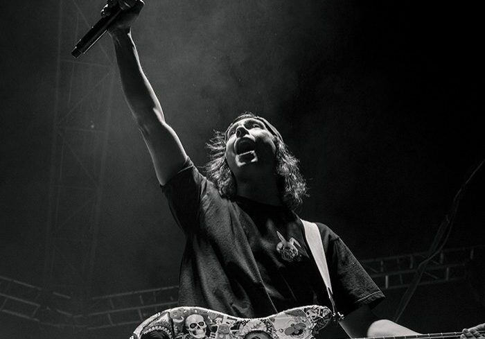 Musician performing energetically with guitar on stage.