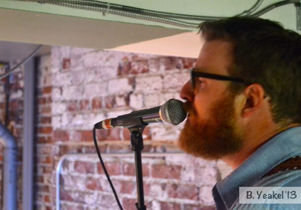 Man singing into microphone, brick wall background.