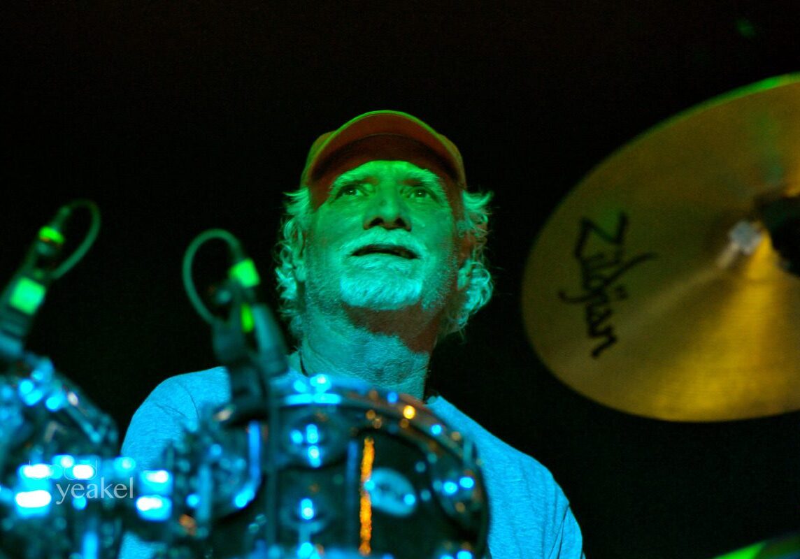 Drummer performing under green stage lights.