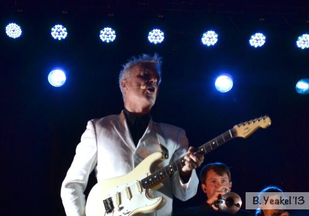 Musician playing guitar under stage lights.