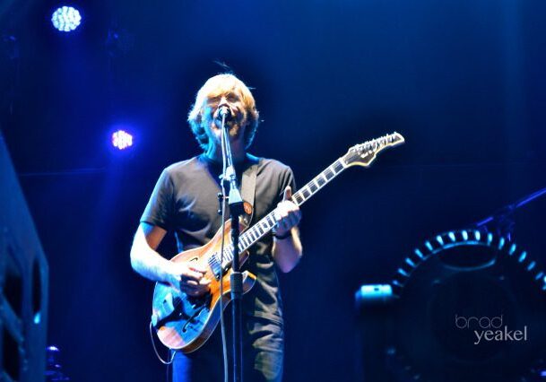 Guitarist performing on stage under blue lights.