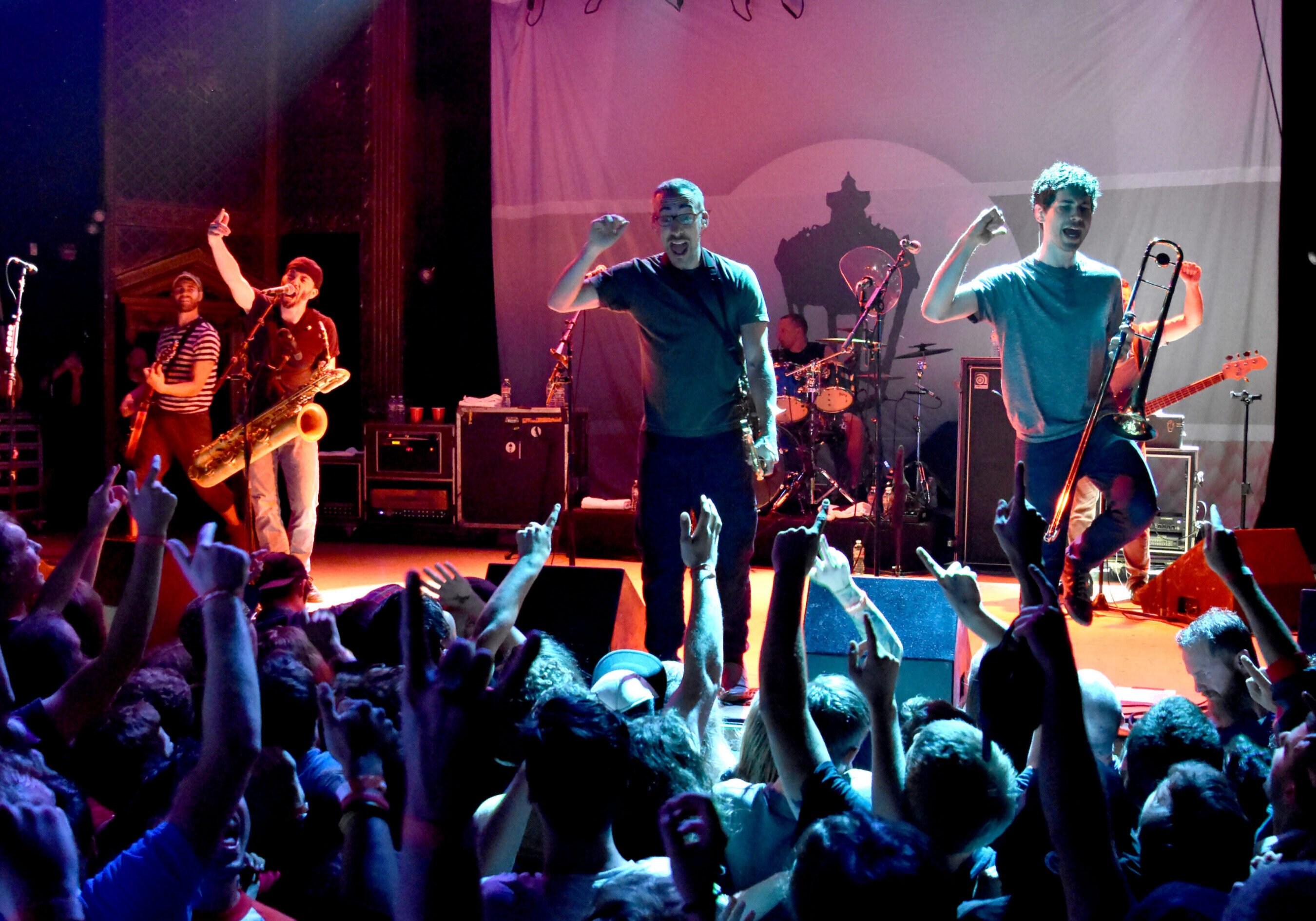 Band performing energetically on stage with audience.