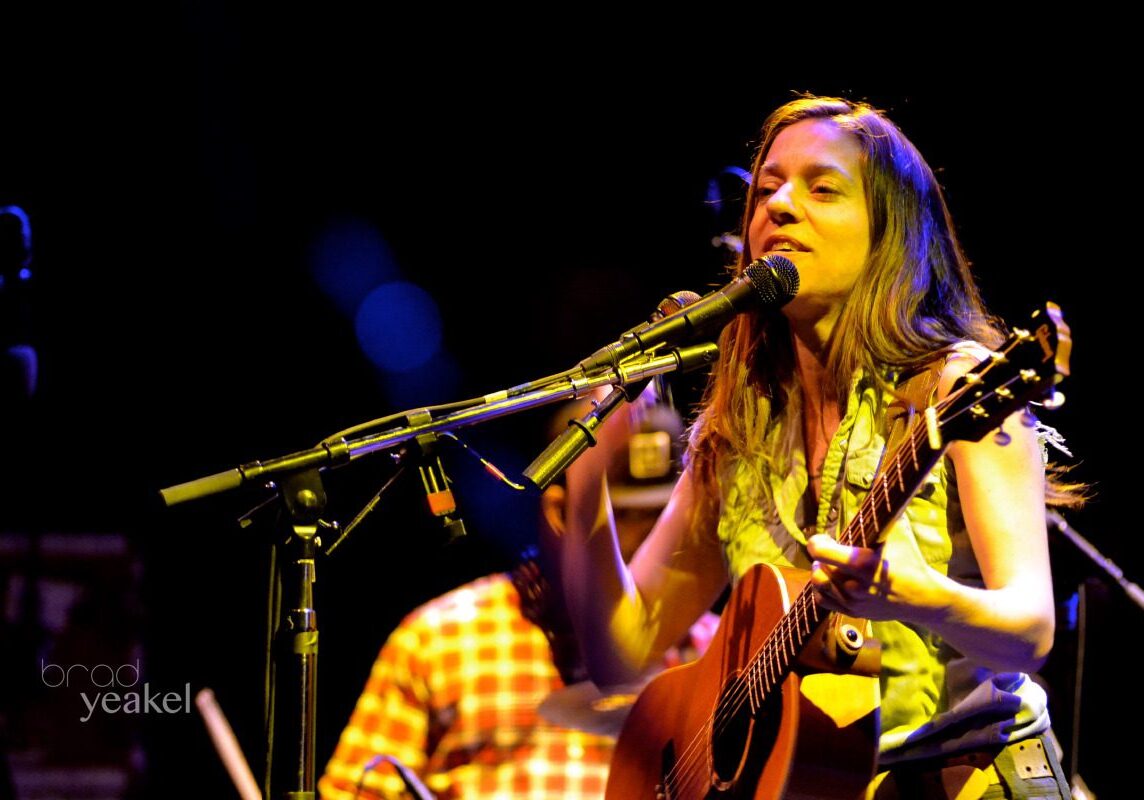 Singer performing with a guitar on stage.