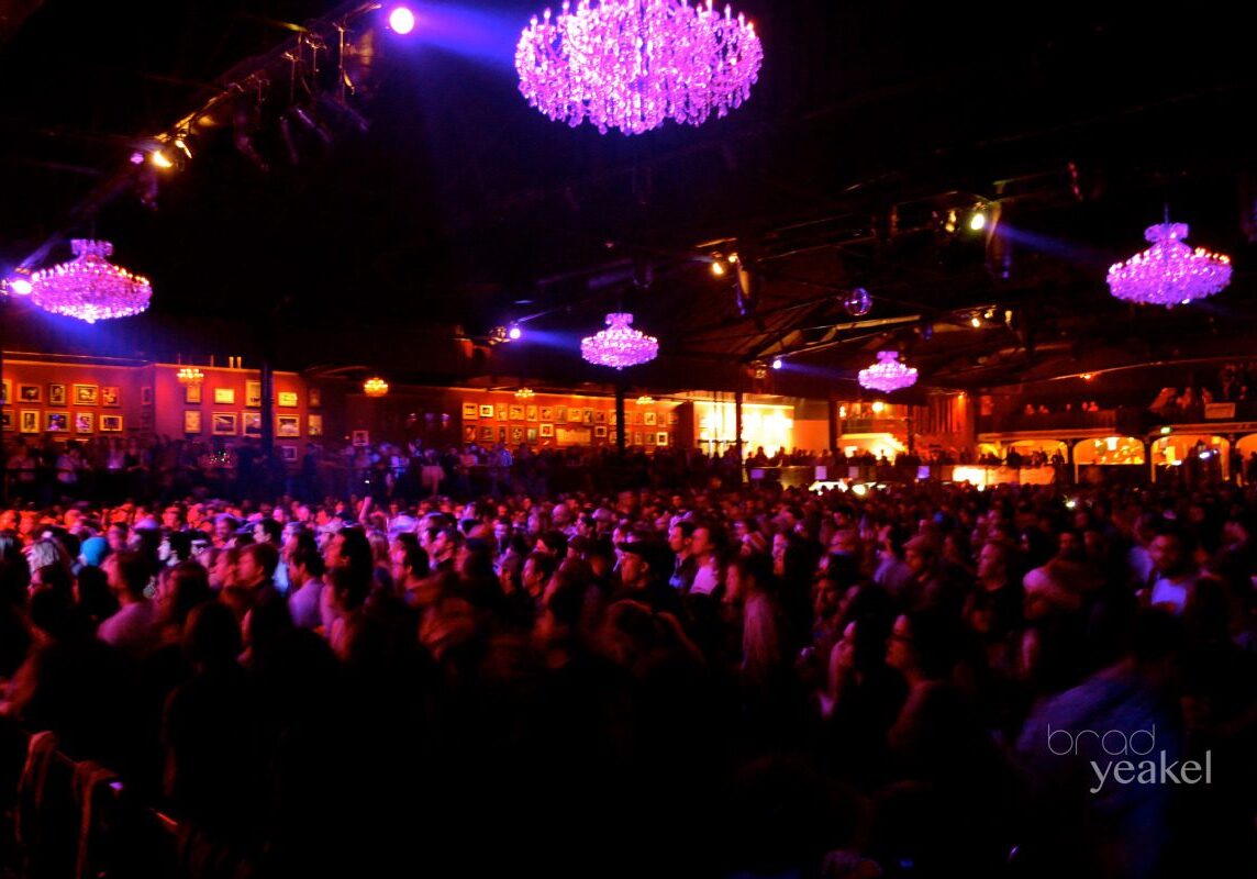 Concert crowd under purple-lit chandeliers.