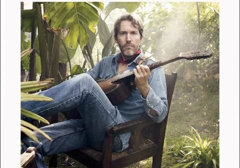 Man playing guitar in a lush garden.