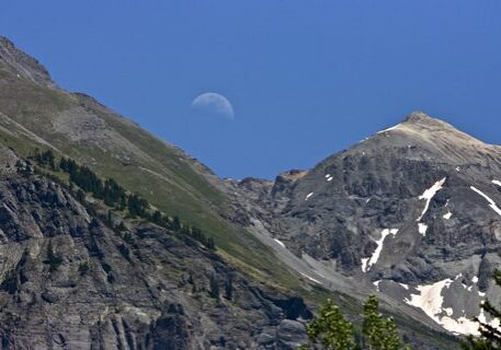 Moon over rugged mountain peaks, clear sky.