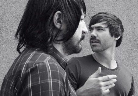 Two men talking against a wall.