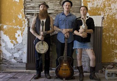 Three musicians with instruments in rustic setting.