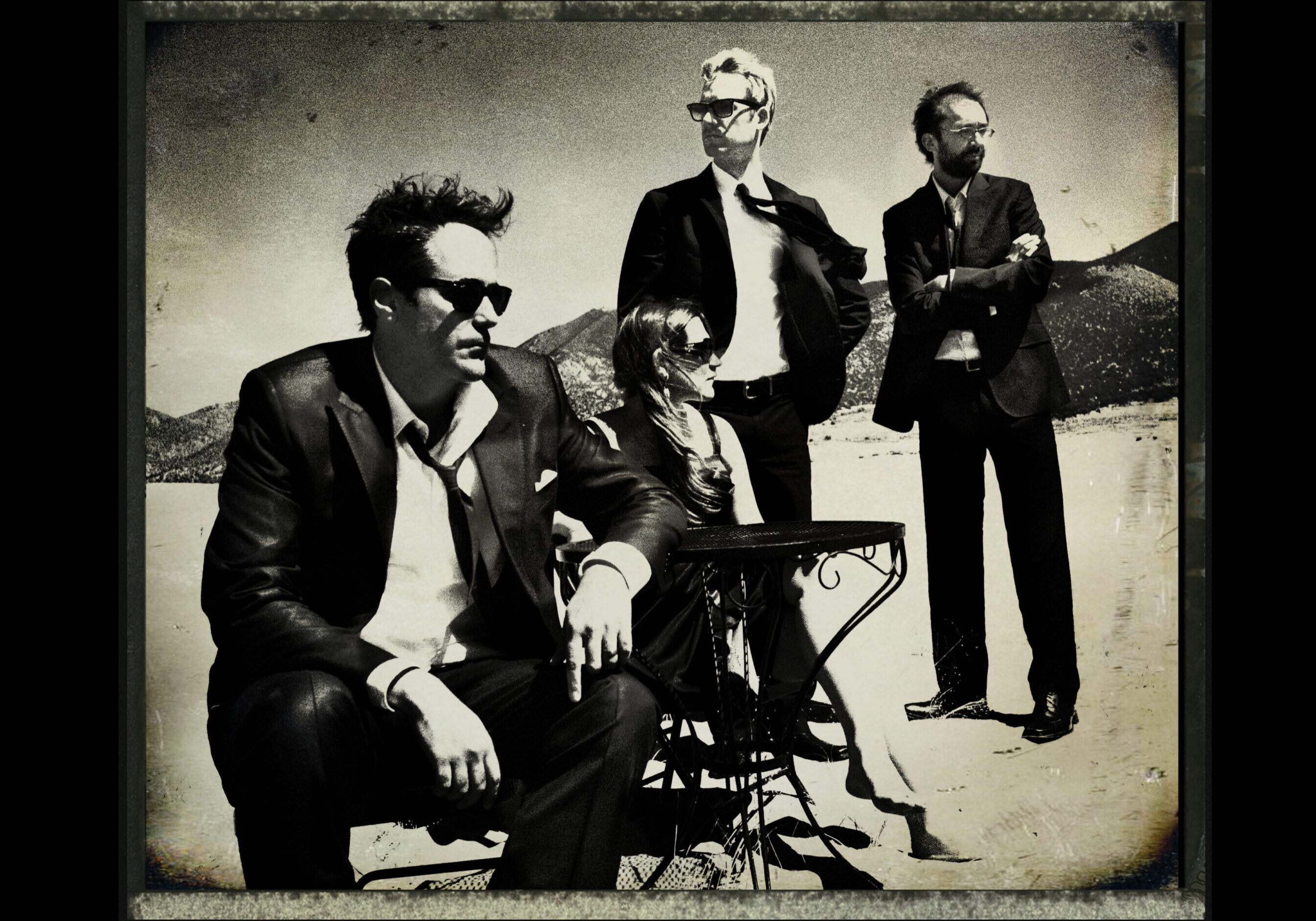 Four people in suits, outdoors, vintage style.