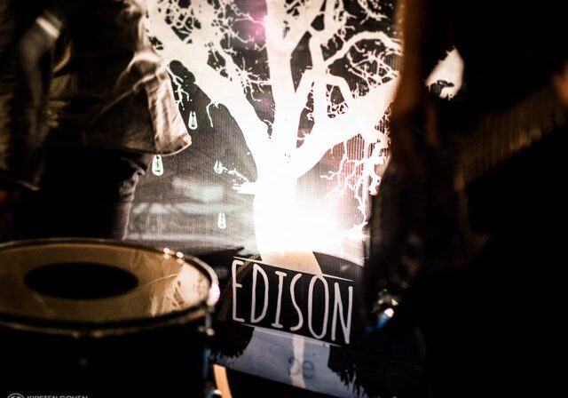 Band performance with drum and illuminated backdrop.