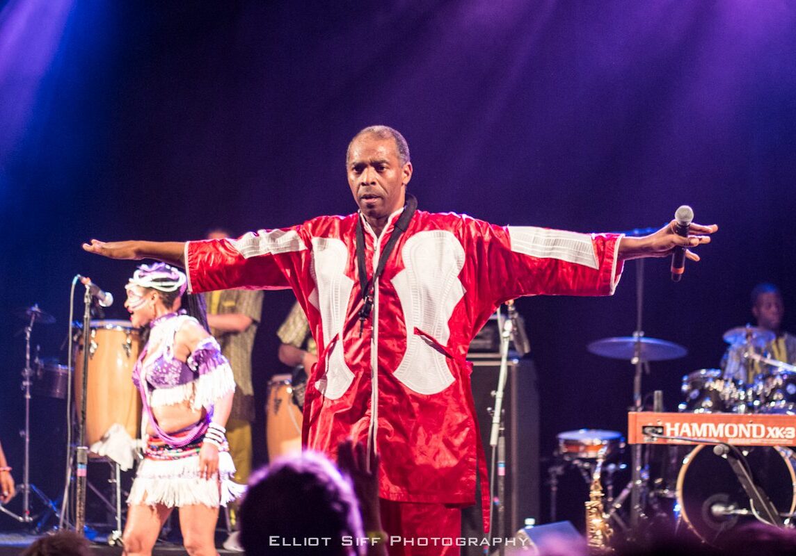Performer in red robe on stage, dancing.