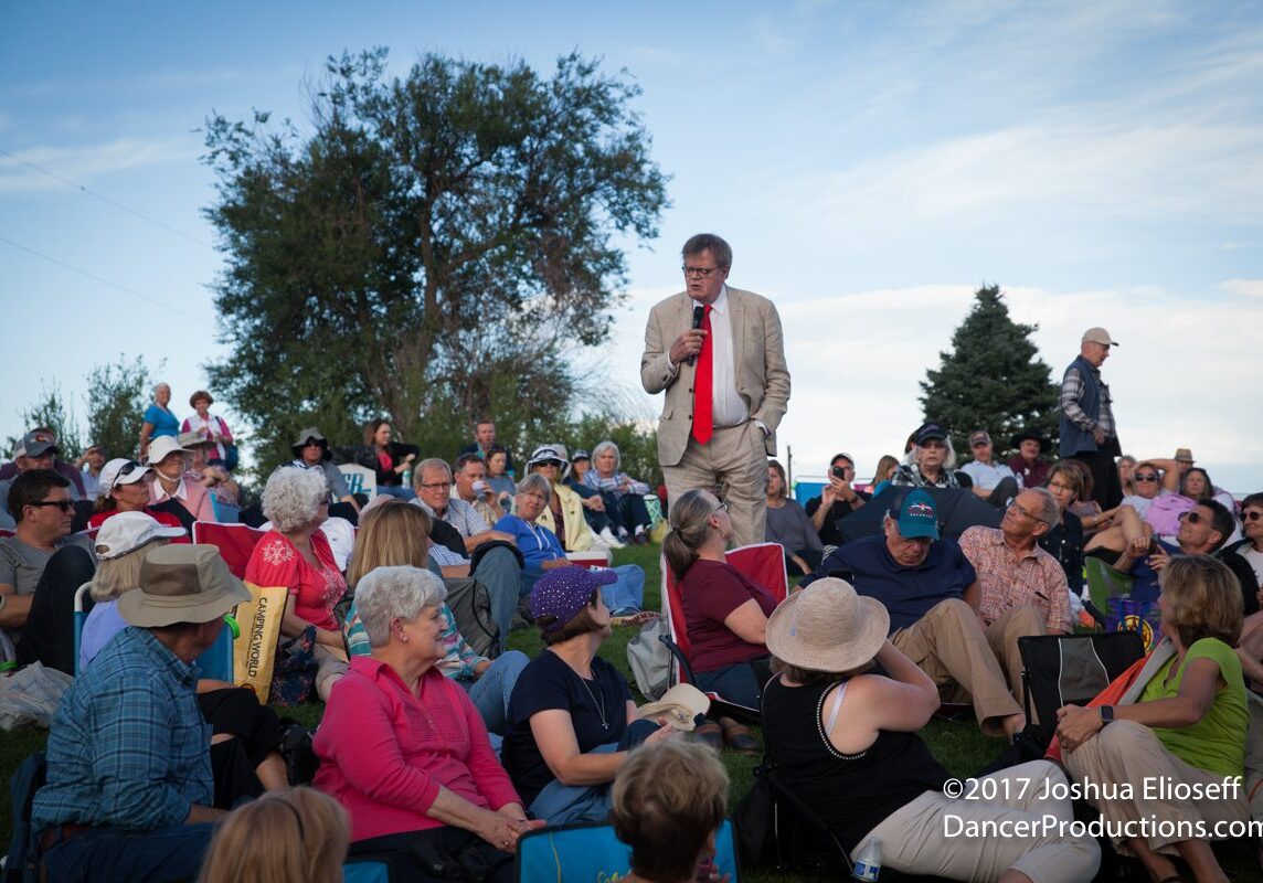Outdoor gathering with speaker addressing seated crowd.