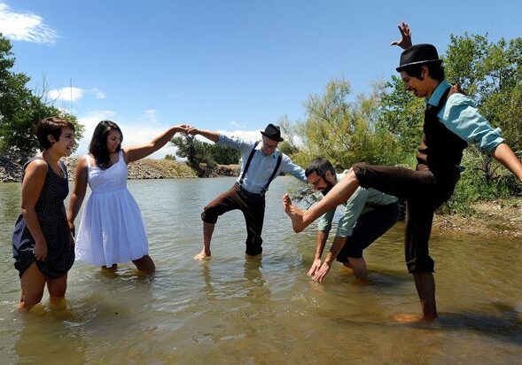 People dancing in a river, wearing hats.
