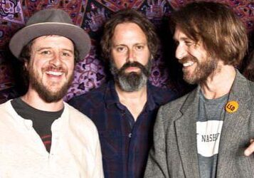 Five men smiling in front of patterned backdrop.