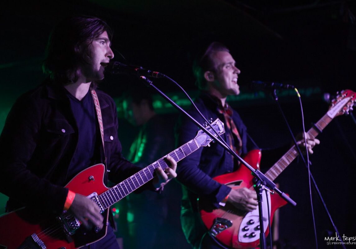 Musicians performing with guitars on stage.