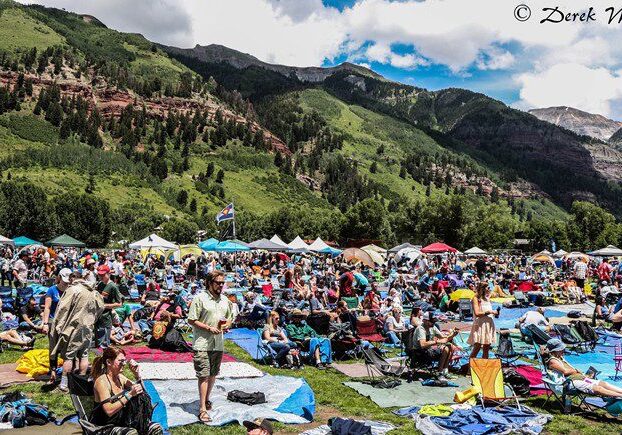 Outdoor festival with mountains and crowd gathering.