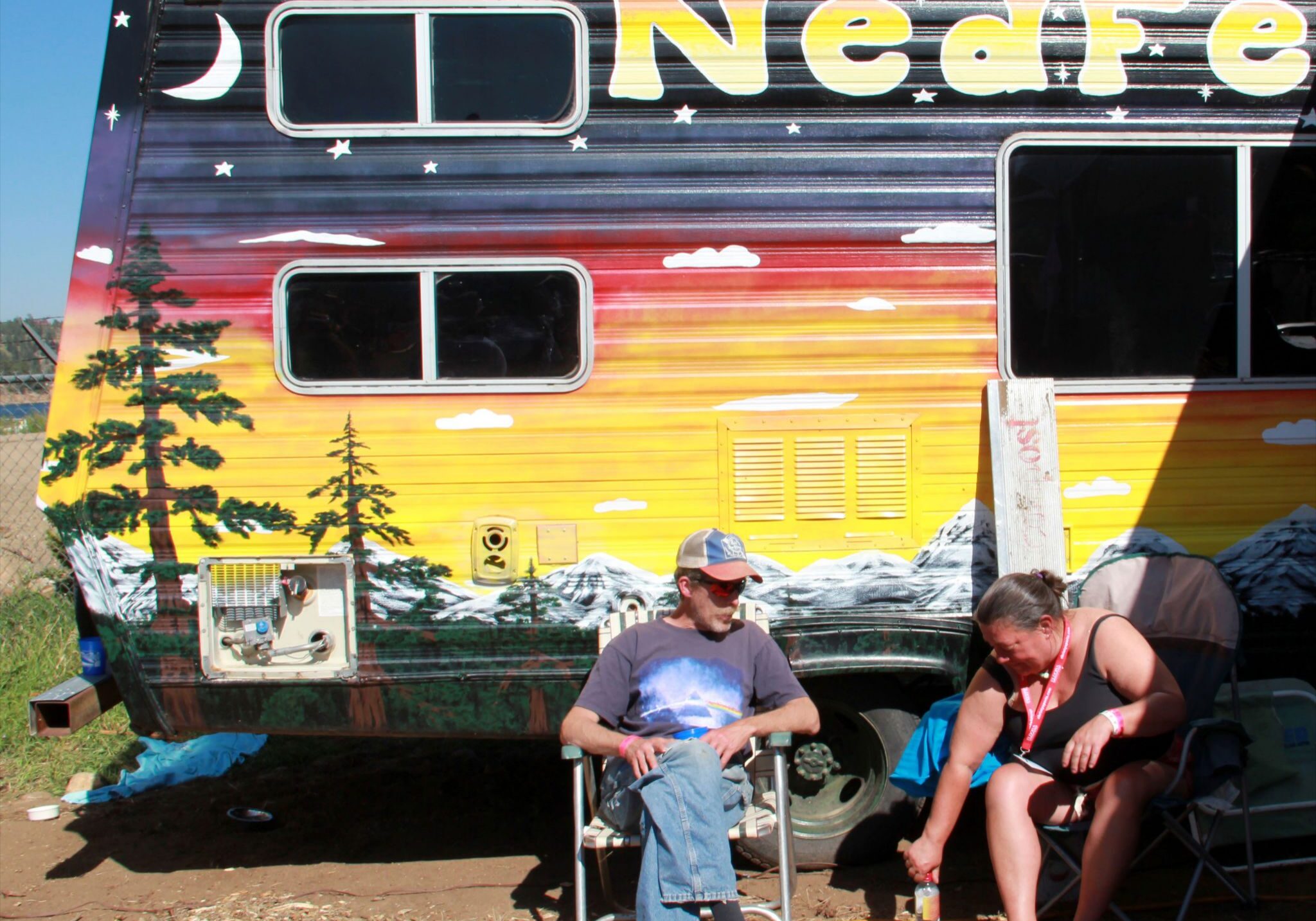 Colorful camper with two people sitting outside.