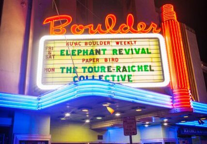 Neon-lit theater marquee with crowd outside.