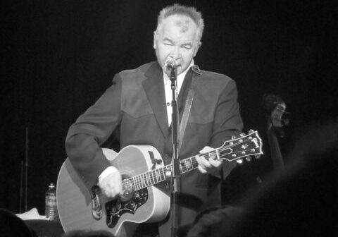 Musician performing with acoustic guitar on stage.