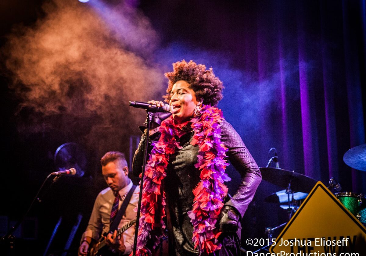 Singer performing energetically on stage with band.