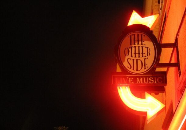 Neon sign reading "The Other Side" illuminated.