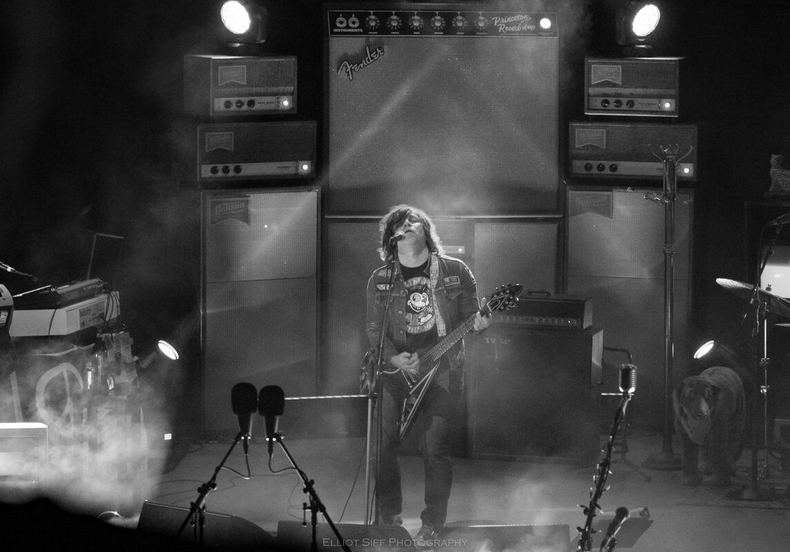 Guitarist performing live on stage with amplifiers.