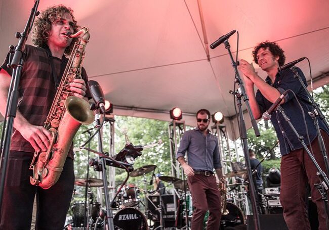 Band performing on outdoor stage with microphones.