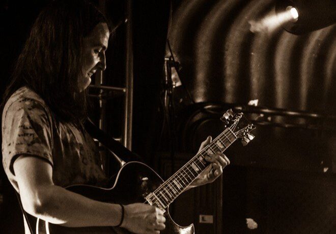 Guitarist playing on stage under spotlight.