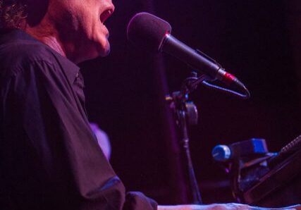 Man singing and playing piano on stage.