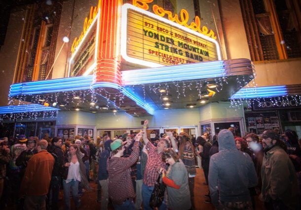 Crowd gathered outside illuminated theater marquee.
