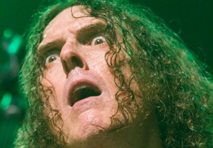 Man with long hair looking surprised, green lighting.