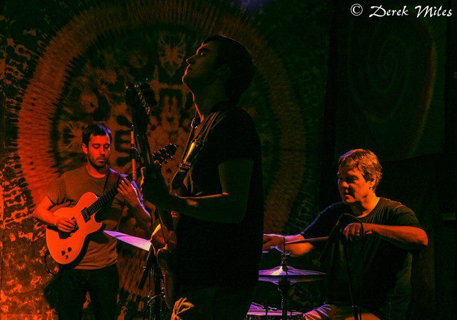 Band performing on stage with guitars and drums.