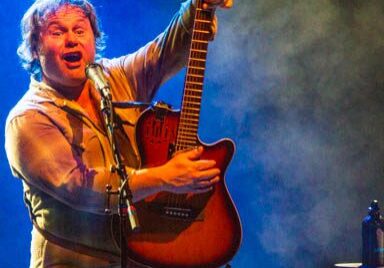 Musician energetically playing guitar on stage.