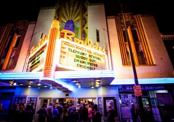 Neon-lit theater entrance with crowd at night.