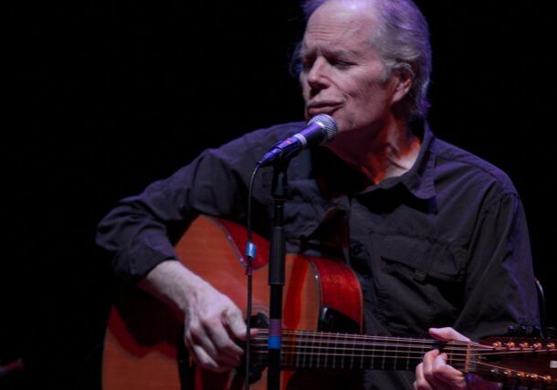 Singer performing with guitar on stage.