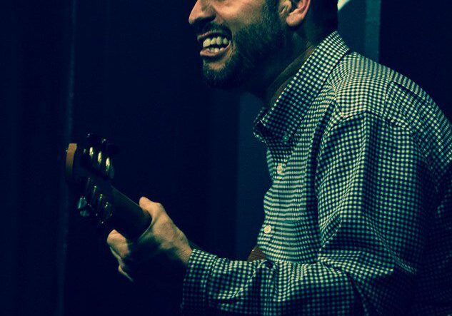 Man playing guitar, smiling on stage.