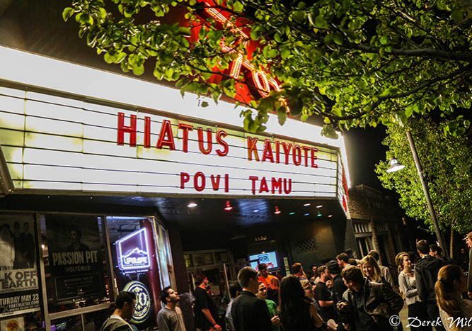 Crowd outside theater with marquee at night.