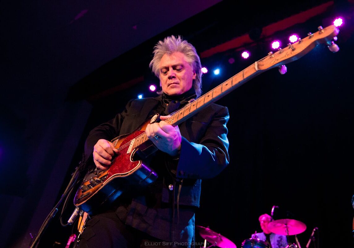 Musician playing guitar on stage with lights.