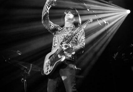 Guitarist performing energetically on stage, black-and-white.