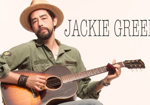 Man playing guitar with hat and harmonica.