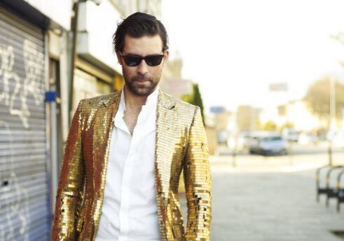 Man in gold jacket and sunglasses walking.