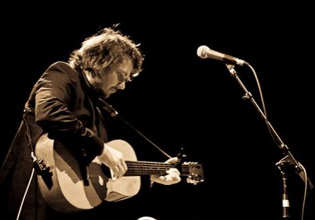 Musician playing acoustic guitar on stage.