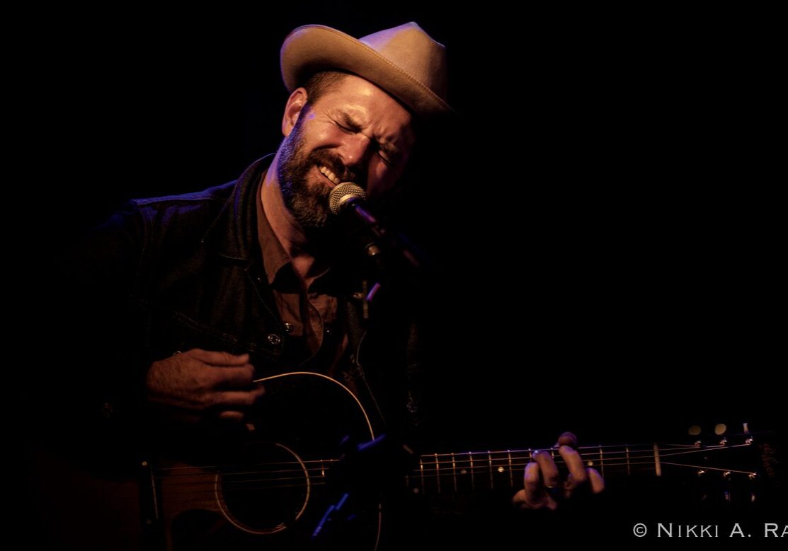 Singer playing guitar on dark stage.