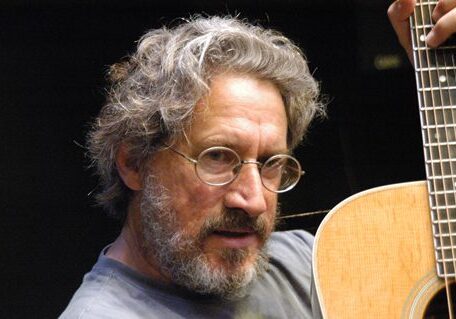 Man holding a guitar, wearing glasses.