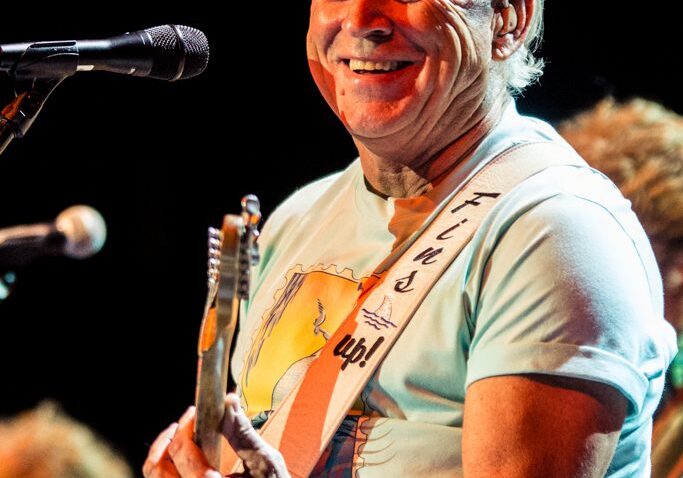 Man playing guitar on stage, smiling brightly.
